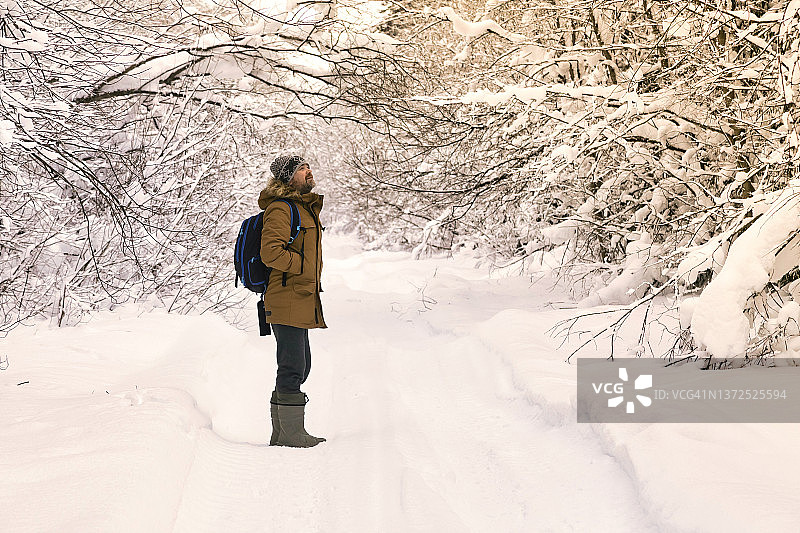 男性徒步旅行者站在积雪覆盖的森林道路中央图片素材