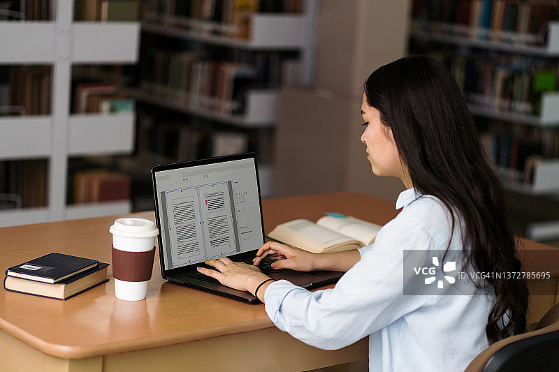女学生坐在图书馆的桌子前，在电脑上打字图片素材
