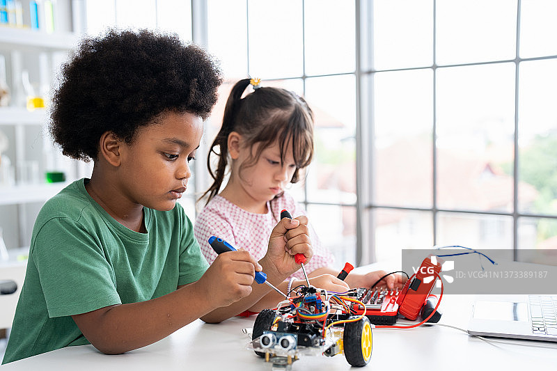 在学校的实验室里，专注的男孩和女孩在创造机器人车。图片素材