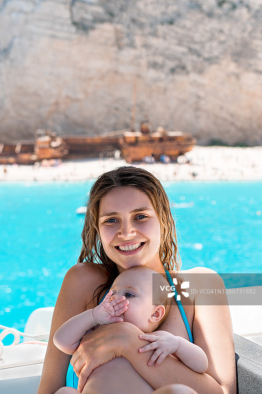 快乐的年轻妈妈抱着可爱的宝宝在海上度假。图片素材