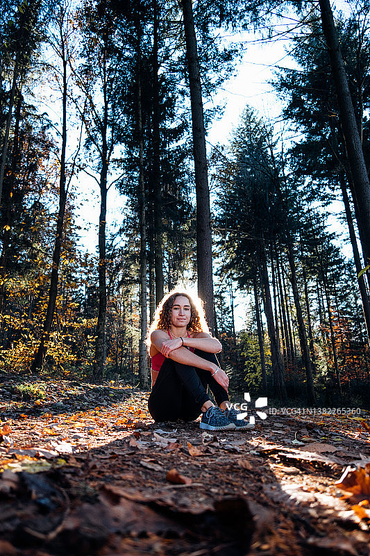 年轻女子坐在秋天的森林阳光下图片素材