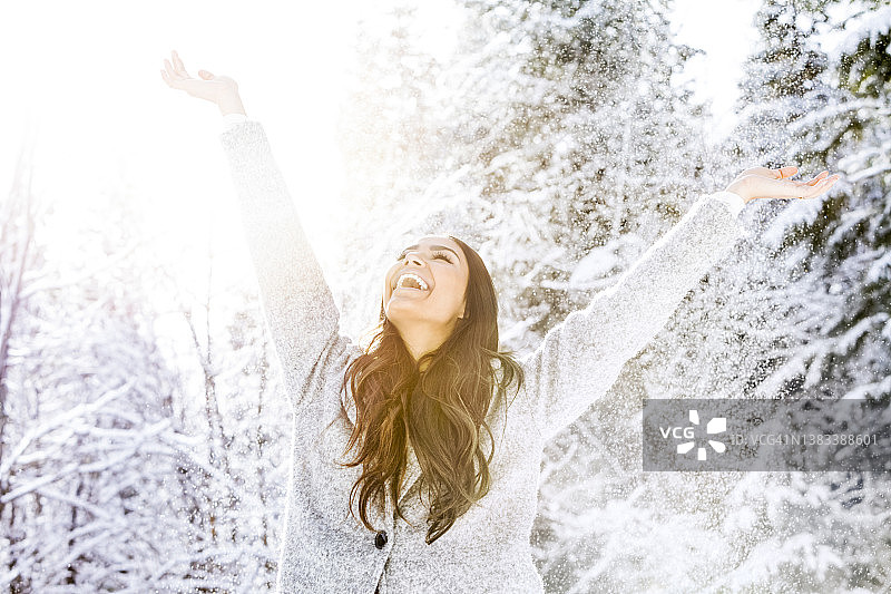 白雪覆盖的森林里，一个快乐的女人举起双臂图片素材