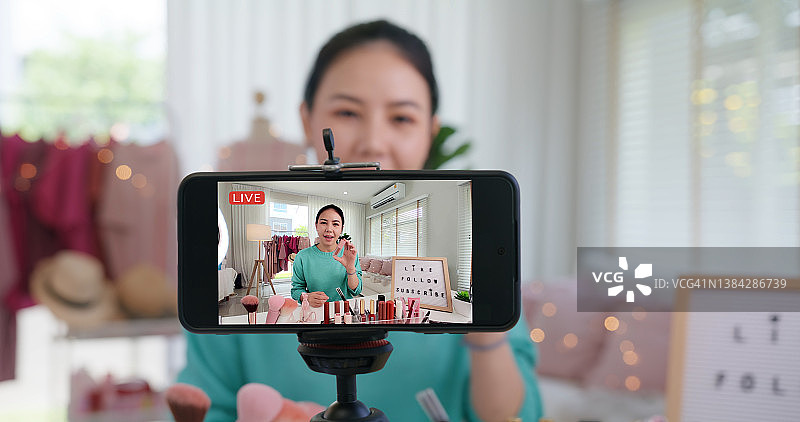 亚洲女性微博网红在家庭工作室录制直播视频。在媒体中快乐的谈笑说笑的建议回顾爱好。视频博主自拍拍摄享受工作展示微笑教像分享应用。图片素材