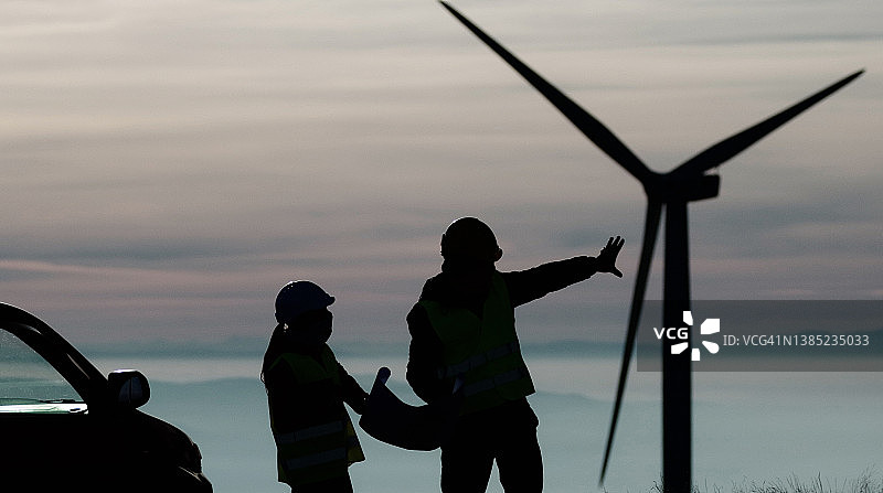 黄昏时分，风能工程师在风电场工作。可再生能源系统。碳中和和可持续能源。图片素材