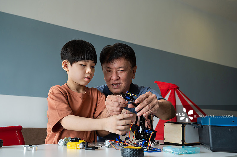 一个年轻的亚洲男孩和他的爷爷在家里一起制作机器人玩具图片素材