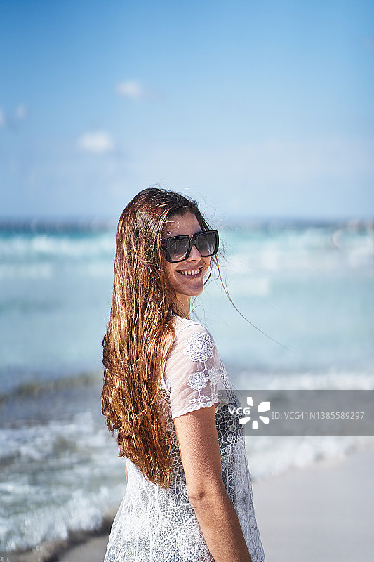 微笑的女人戴着太阳镜，穿着沙滩服站在海边图片素材