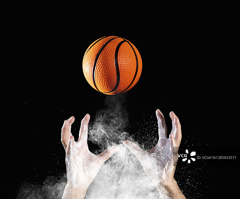 一个篮球运动员的手在黑色的背景上接住了一个球。图片素材