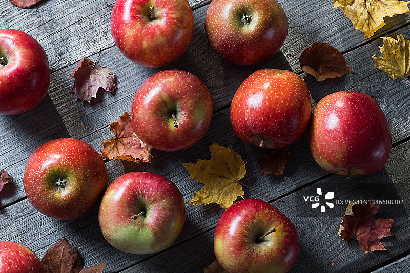 红色的苹果和秋天落下的黄叶桦树，枫树和白杨在木制的背景上。厨房桌子上的水果。有机农产品的种植。素食的概念，纯素，生食和饮食。秋天的自然背景。收割。图片素材