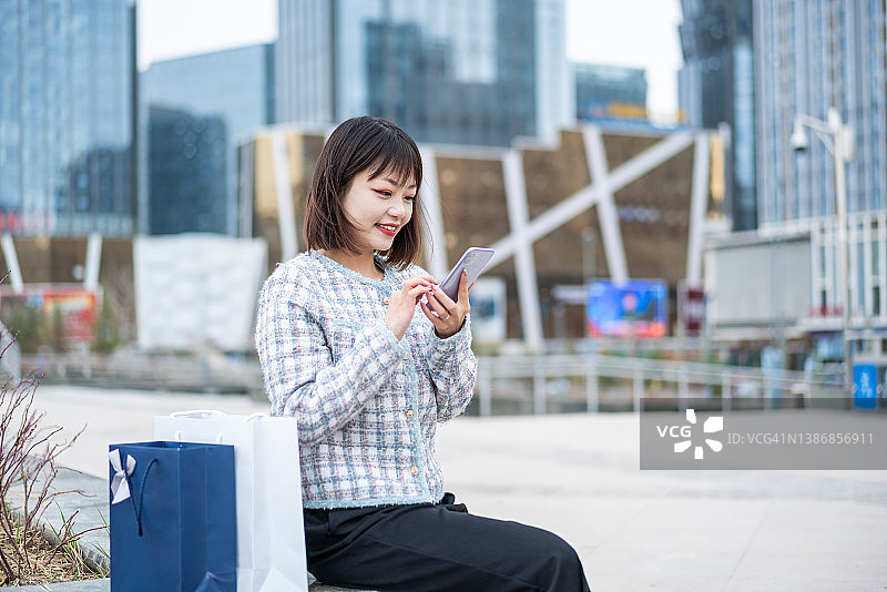亚洲年轻女子购物后在城市街道使用智能手机图片素材