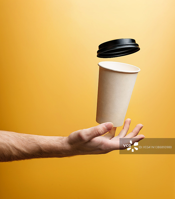 一个装热饮的纸杯悬浮在一个男人的手掌上，特写镜头。图片素材