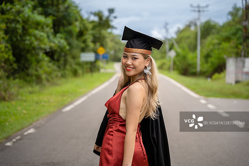 美丽优雅的年轻女毕业生穿着红色的裙子，把她的毕业礼服扛在肩上图片素材