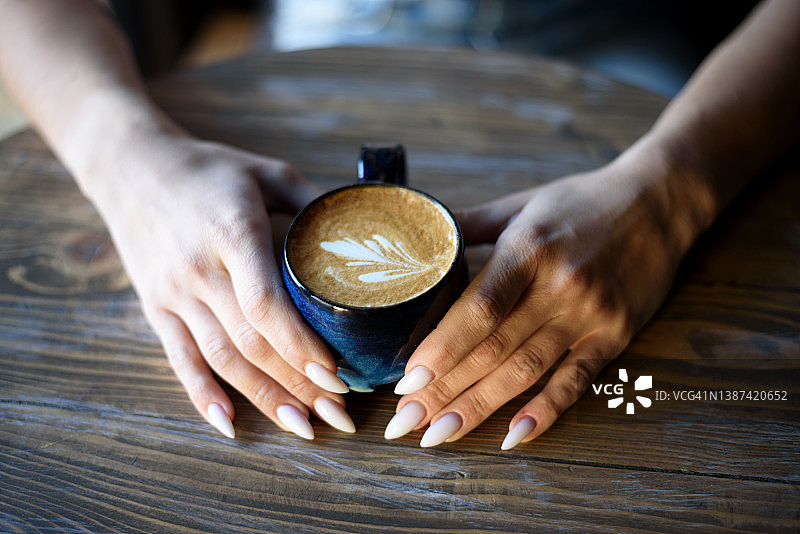 近距离拍摄美丽的女性手握大杯黑色的卡布奇诺咖啡。从上面拍摄，俯视图。图片素材