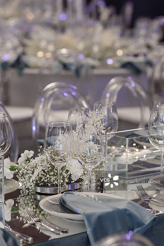 餐桌上摆放着昂贵的餐具，盘子上有蓝色的餐巾，白色的花，蜡烛，玻璃杯。图片素材
