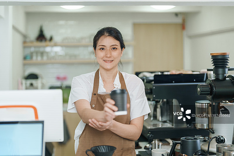 年轻的亚洲女服务员在咖啡店工作。服务员端着咖啡杯给顾客。当地的小生意。年轻企业主。图片素材