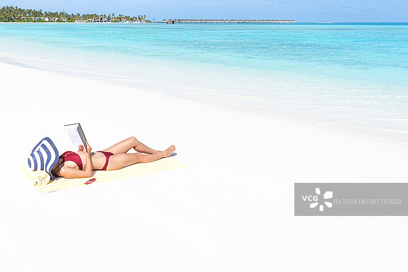 年轻迷人的女人在热带海滩读书图片素材