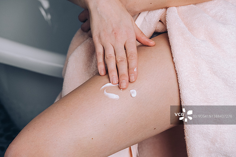 妇女在大腿皮肤上涂保湿乳液，沐浴后涂身体霜图片素材