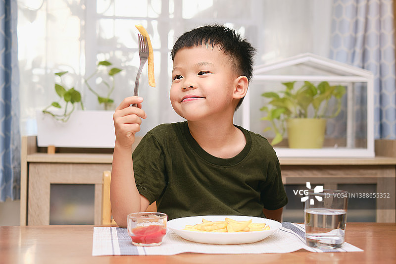 快乐的亚洲幼儿园小男孩用叉子吃薯条薯条和番茄酱图片素材