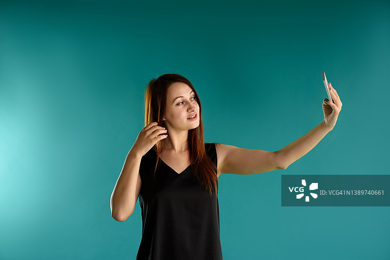 在蓝色背景上，一名快乐的红发年轻女子享受着移动通信和现代技术。为您的广告内容提供免费空间。图片素材