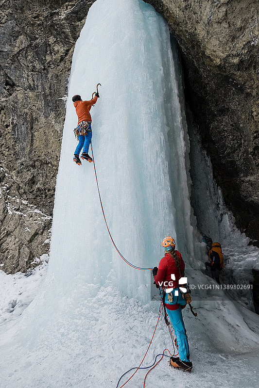 一名冰上攀岩者在他的同伴保护下爬上陡峭的冰冻瀑布图片素材