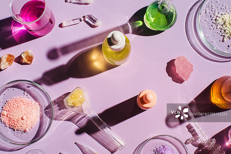 色彩鲜艳的背景与实验室用具，化妆品样品和玻璃瓶在紫色的背景。天然药物、美容研究、生物科学、有机护肤品。俯视图，平躺。图片素材