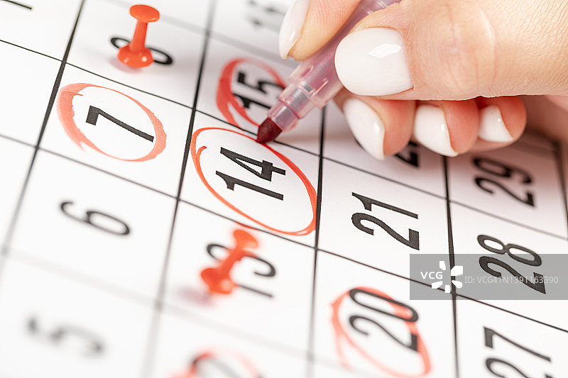 贴近员工女性的手，用红笔在日历上写下2022年的日程安排，预约会议或管理每天在家工作的时间表概念图片素材