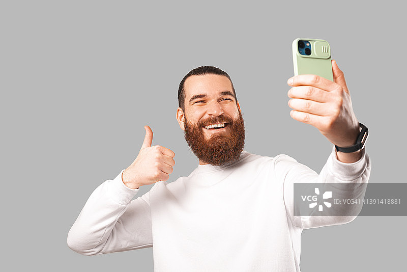 一名大胡子男子正狂喜地拿着手机自拍。图片素材