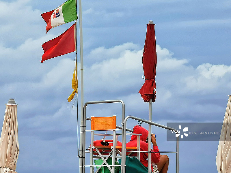 救生员站在海滩上，意大利国旗在风中飘扬图片素材