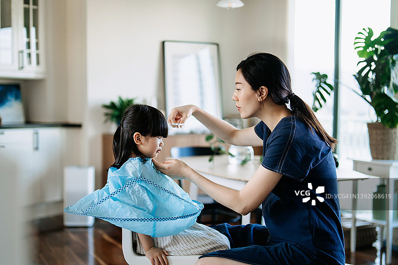 年轻的亚洲母亲在家里给她的小女儿剪头发图片素材
