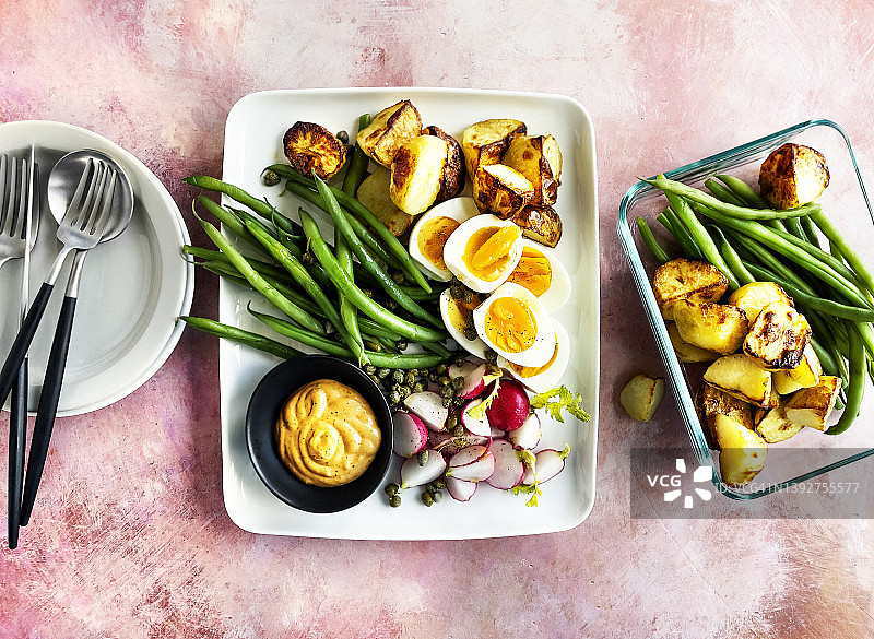开胃菜盘(青豆，萝卜，煮熟的鸡蛋，烤土豆和蒜泥蛋黄酱)，粉红色的背景图片素材