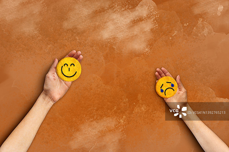 概念图像人类的手握悲伤和快乐的表情符号在棕色的背景图片素材