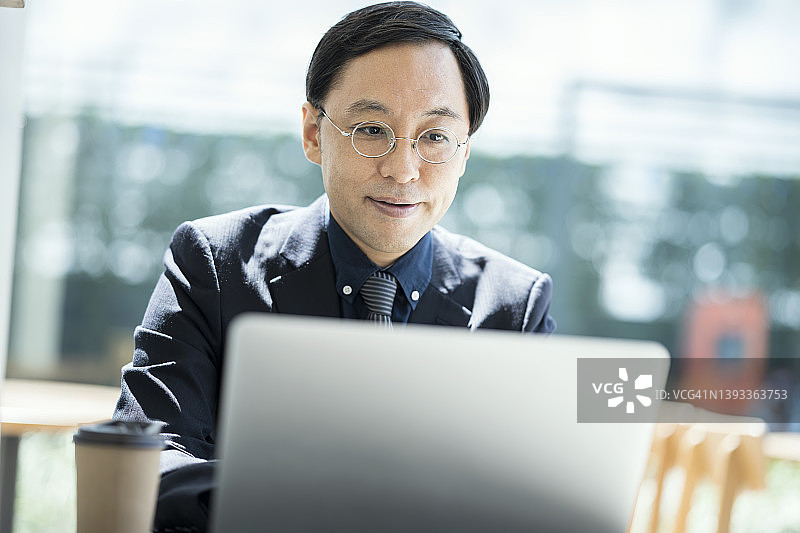 在现代商业大厦的大厅里，一位资深的日本商人正在用笔记本电脑与客户进行商业数据决策。图片素材