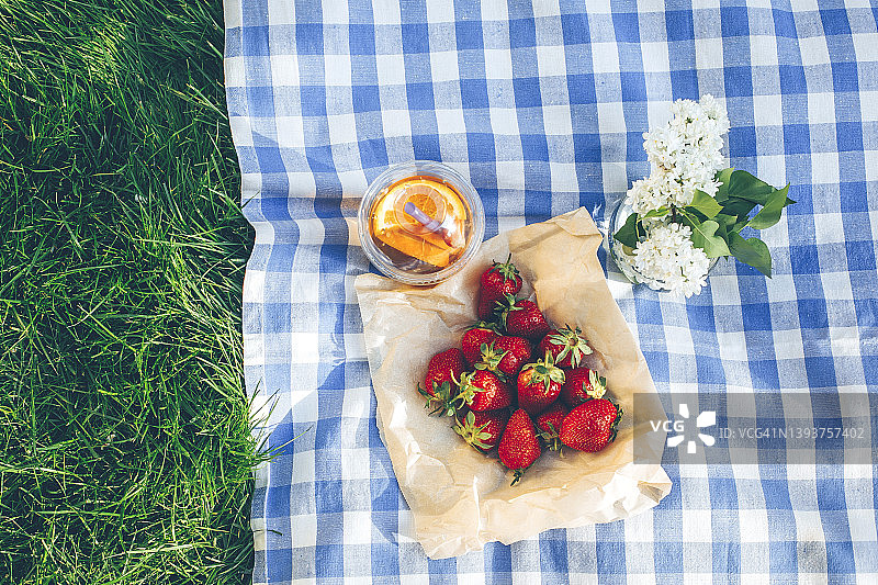 俯瞰野餐毯。新鲜成熟的草莓，外加一杯柠檬水。在公园草地上的户外野餐图片素材