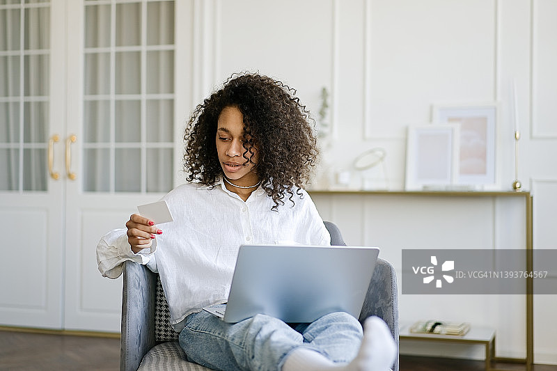 非洲裔美国女孩使用笔记本电脑在家里用信用卡在线购物图片素材