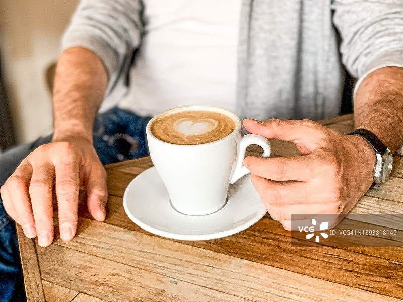 年轻人正在喝咖啡在咖啡馆白色陶瓷杯与茶托在木桌图片素材