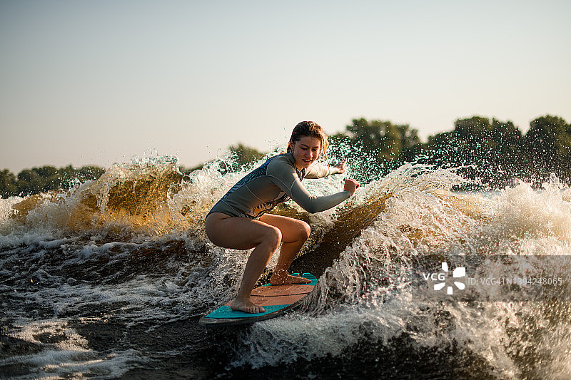 微笑的湿女人水上冲浪骑在飞溅的波浪在温暖的一天图片素材