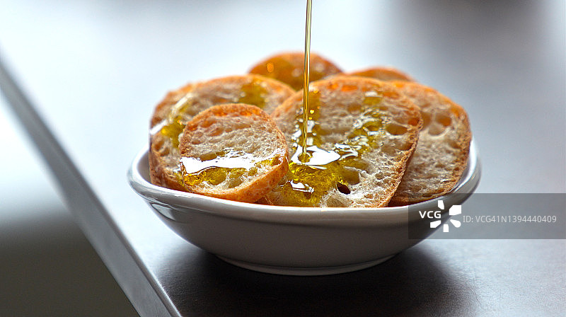 脆皮的乡村切片法国法棍面包淋上橄榄油。图片素材