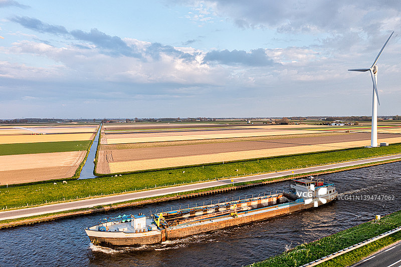 一艘船在运河上的鸟瞰图，旁边是五颜六色的郁金香田——荷兰图片素材