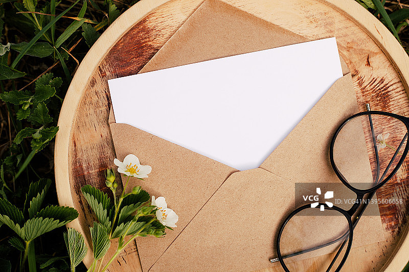 信封与空白白纸卡拷贝空间的木制板，眼镜对绿叶和花卉花卉背景图片素材