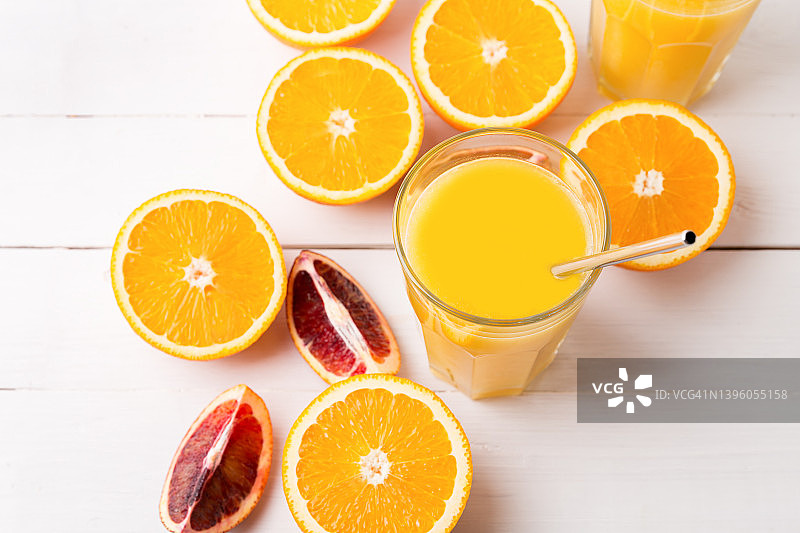 两杯新鲜的果汁，成熟的新鲜橙子放在白色的木桌上。图片素材