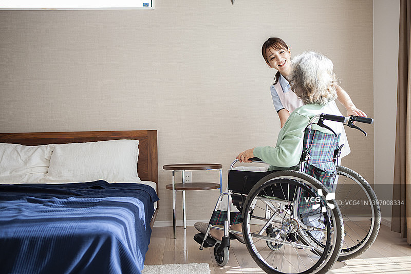 一位护理人员牵着一位坐轮椅的老妇人的手，温柔地和她交谈。图片素材