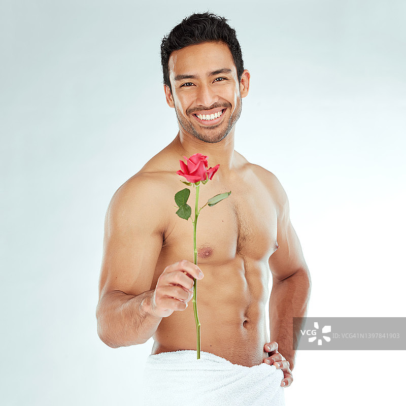 一个有魅力的年轻男子拿着一朵玫瑰，背景是工作室图片素材