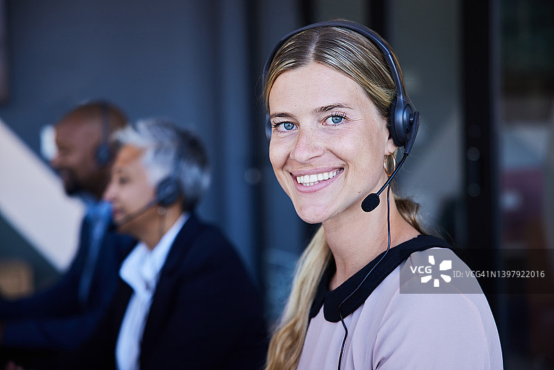 微笑的年轻女性客服代表戴着耳机在办公室工作图片素材