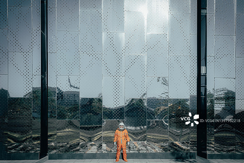 身穿橙色太空服、头戴太空头盔的宇航员站在太空中心大楼附近的户外。图片素材