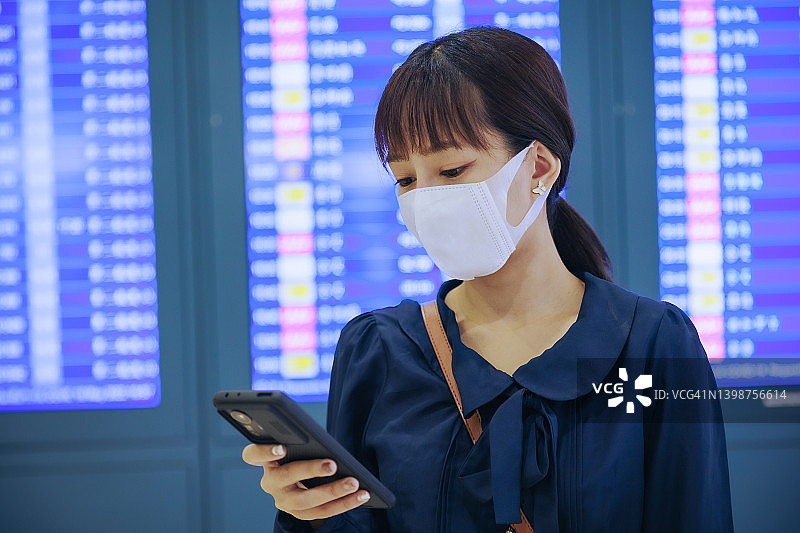 年轻的亚洲女企业家们戴着口罩，在机场登机牌前阅读电子邮件。商务旅行的概念。图片素材