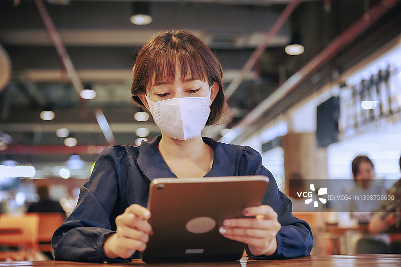 年轻的亚洲女商人戴着口罩在机场出境区工作或用数字平板电脑阅读电子邮件。商务旅行的概念。图片素材