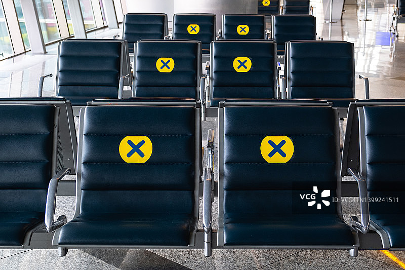 在机场的椅子上贴上黄色标志的新贴纸，与其他乘客保持一个座位的距离。保持距离，保护和预防COVID-19冠状病毒的传播风险。隔离和大流行期间免费座位。图片素材