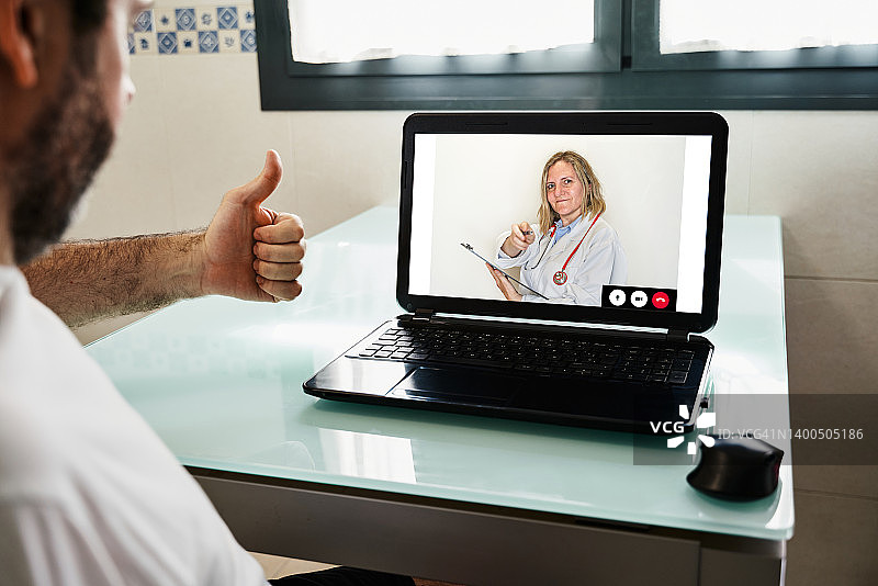 一名白人男子在家中用笔记本电脑在线医疗数字技术服务咨询与生病的医生进行视频通话的背影。图片素材