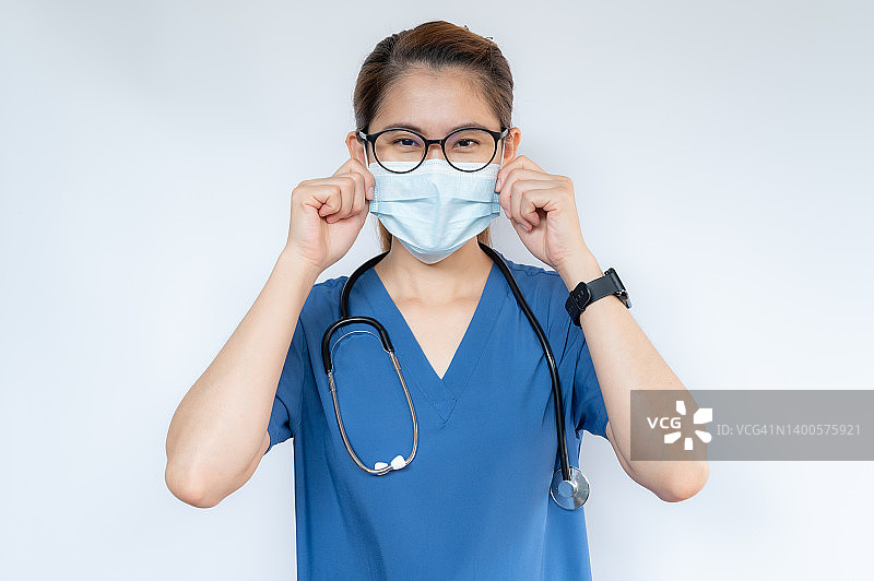 白色背景上隔离的身穿蓝色医用消毒衣、戴着外科口罩的医护人员在医院工作前的肖像。图片素材