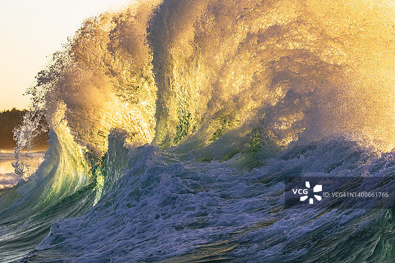 狂暴的海浪危险地冲破海岸，被明亮的金色晨光照亮图片素材