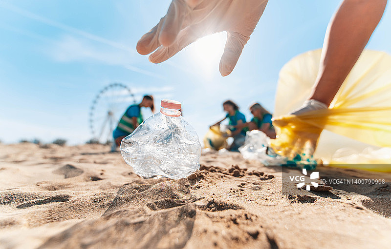 沙滩上捡拾塑料垃圾的生态志愿者团体——捡拾垃圾的积极分子保护地球——海洋污染、环境保护和生态理念图片素材